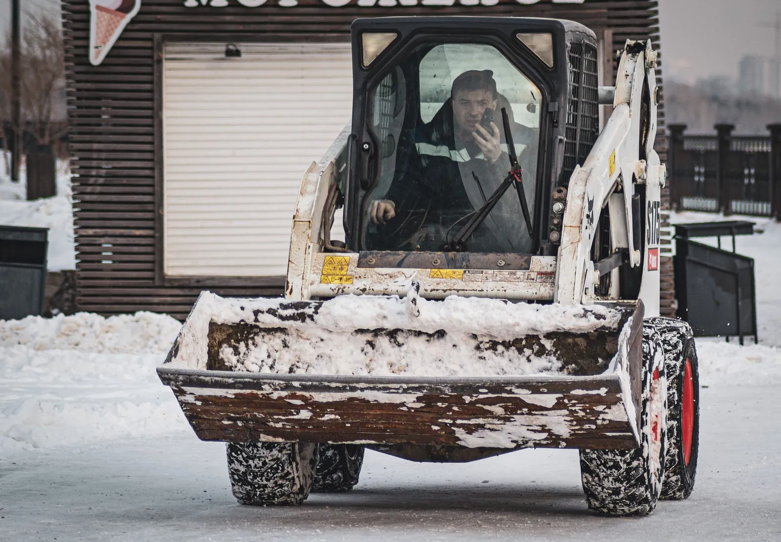 A skid steer with a snow bucket in front of a garage door