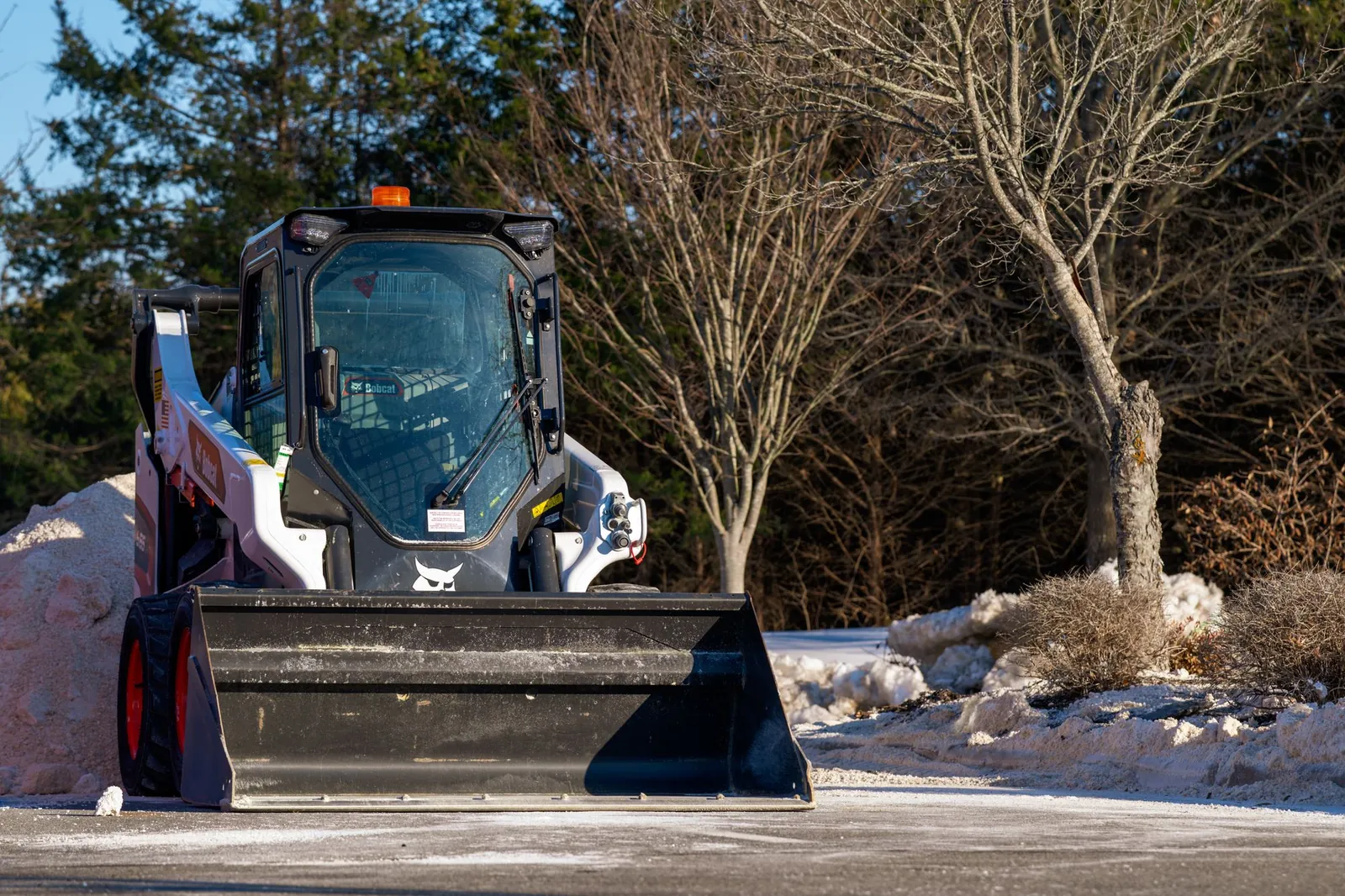 A skid steer with a bucket clearing snow from a parking lot